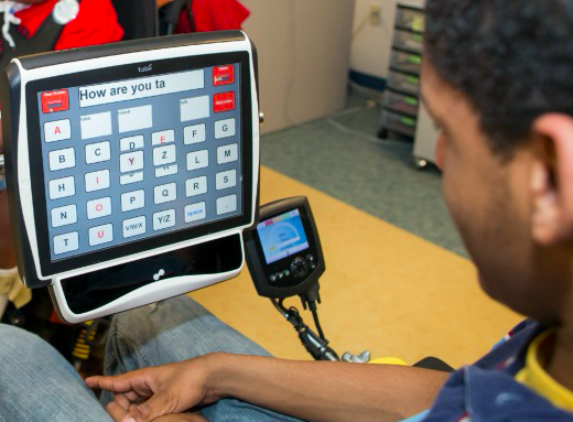 A photo of a person in a wheelchair typing a message on his augmentative and alternative communication (AAC) device.